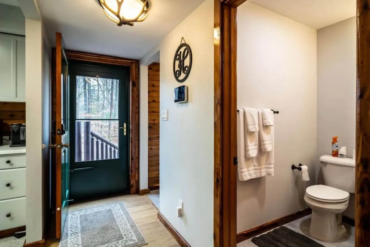 This image captures the main front door area, blending an inviting entrance with glimpses of the home’s welcoming bathroom and decorative wall art. The space feels like a threshold between indoors and out, suitable for greeting friends as they arrive for a retreat or group getaway.