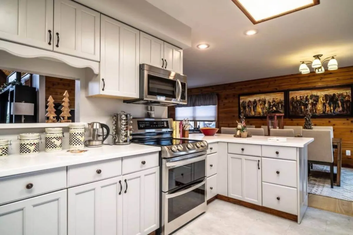 A cozy, inviting kitchen featuring modern stainless steel appliances, sleek white cabinetry, decorative jars, and eye-catching artwork on the wall. The layout offers plenty of counter space for food prep and group cooking, with enough room for multiple people to participate.