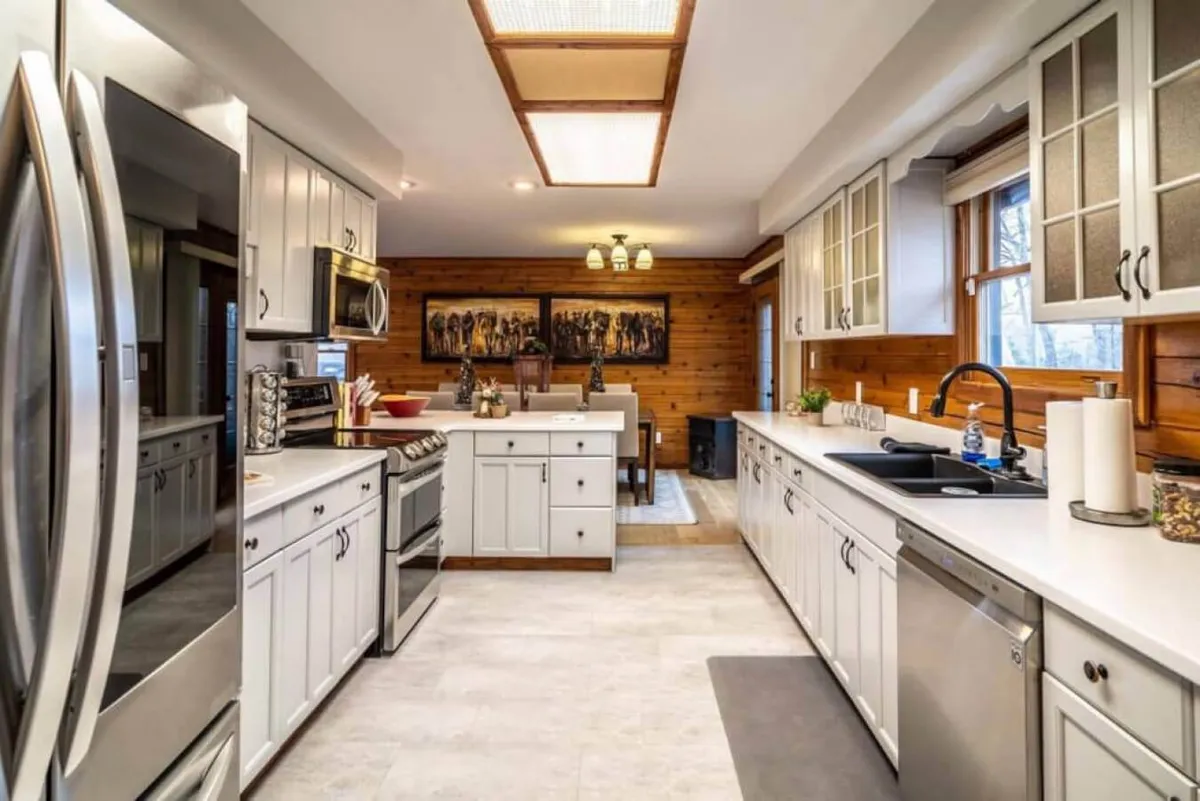 A view integrating both the kitchen island and adjacent dining area, with modern stainless steel appliances, wooden wall art, and a seamless connection between the two spaces. The open layout encourages interaction and easy movement between prepping, cooking, and dining.