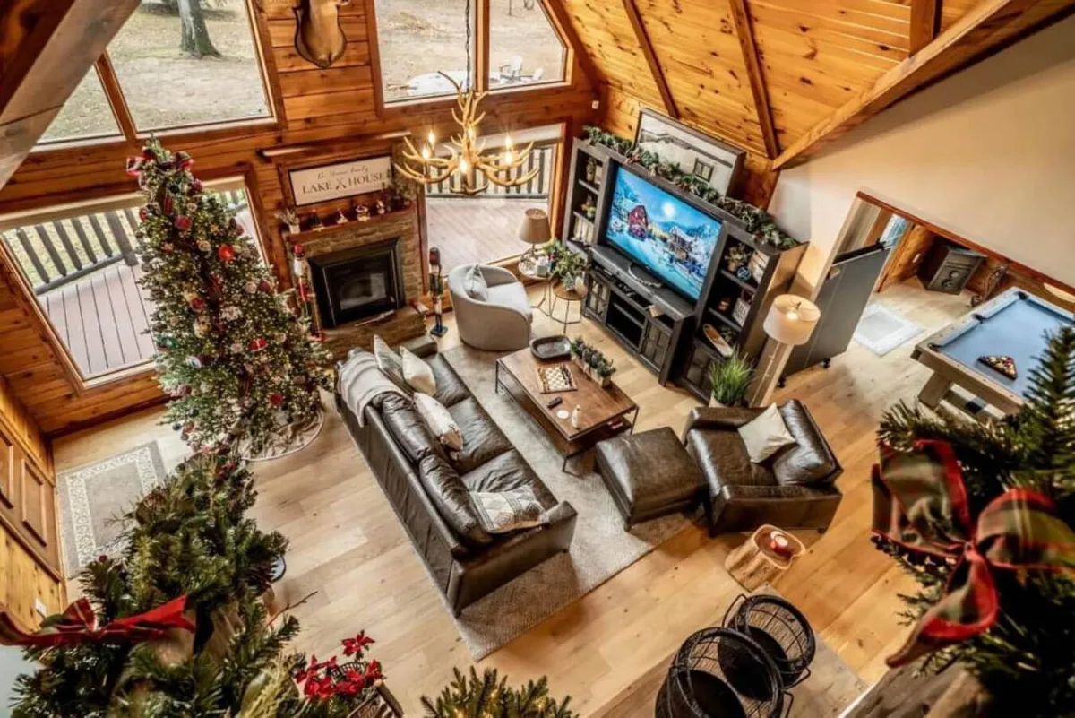 A warm, inviting living room complete with a large Christmas tree, plenty of comfortable seating, a fireplace, and a chandelier above. The scene is set for family gatherings, holiday celebrations, and evenings of storytelling.