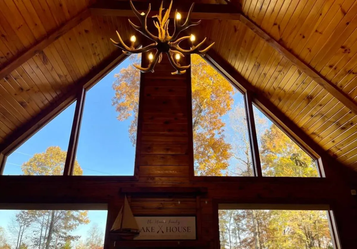 A spacious area with large windows displaying beautiful views, a chandelier overhead, and wooden paneling for rustic charm. The room is designed for gatherings, relaxation, or game nights, with seating that encourages social interaction and appreciation of the outdoors from within.