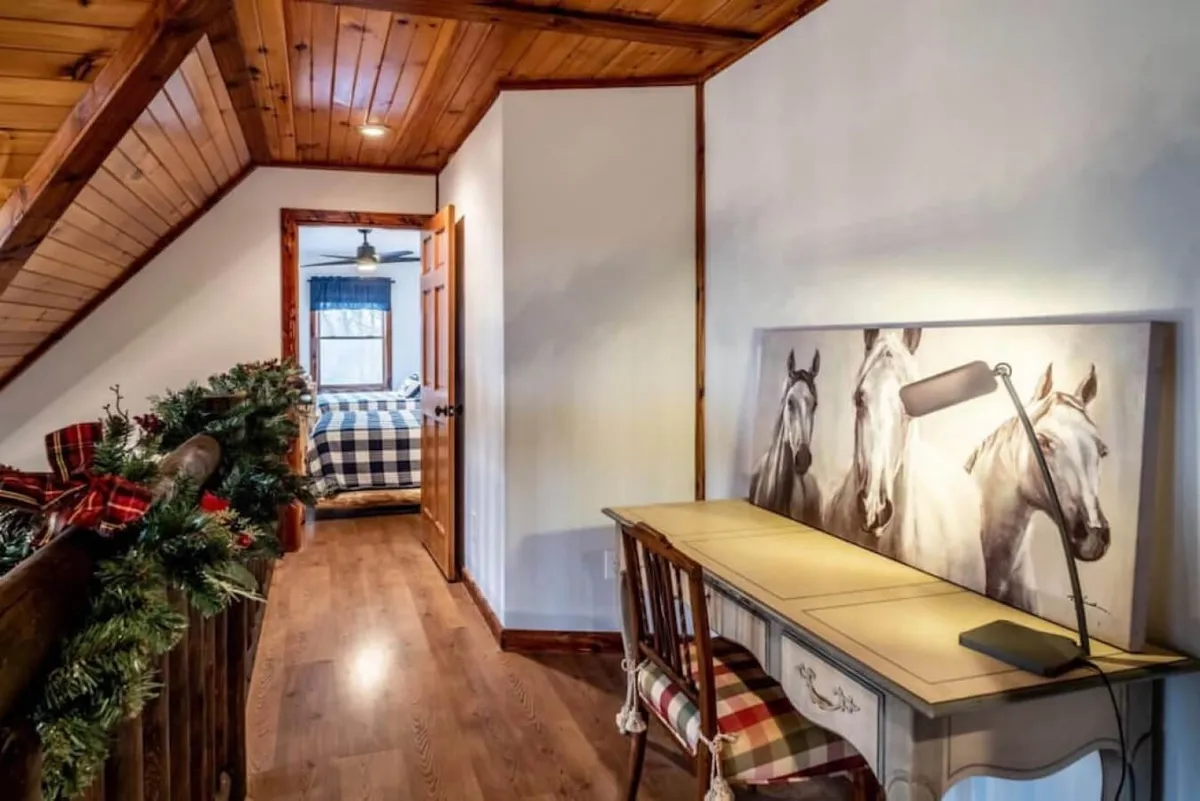 The image showcases a wooden staircase, a desk with horse artwork, and a decorative garland. The tranquil, warm mood and holiday décor suggest seasonal transitions and family traditions, with a hint of the outdoors through the staircase leading to new spaces.